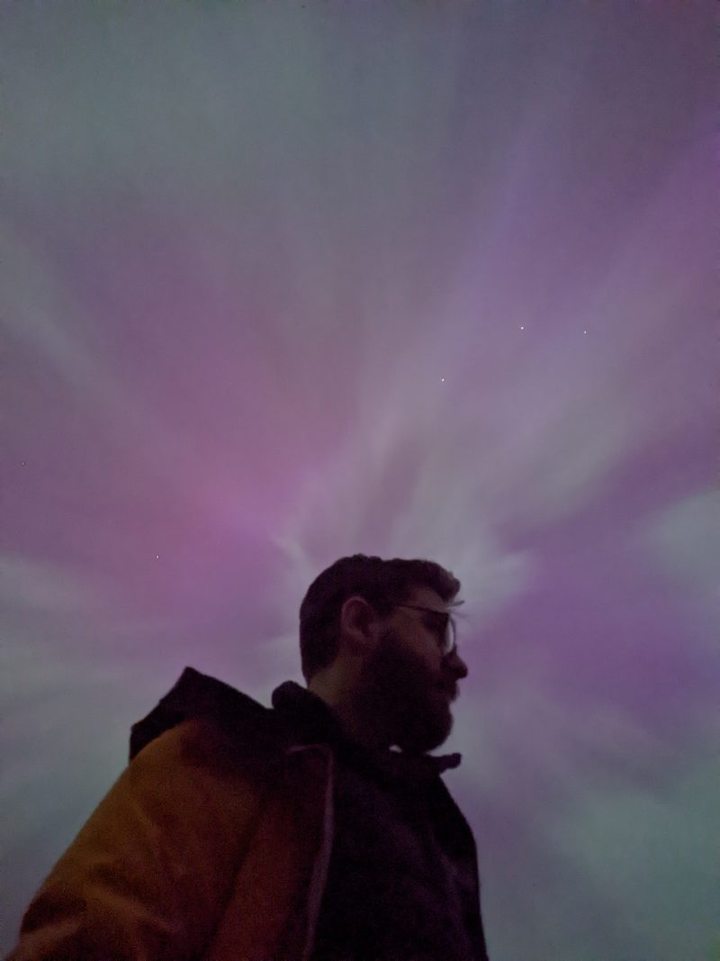 Alex in profile against a purple and green aurora sky